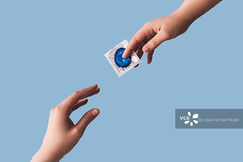 蓝色背景下手递手传递蓝色避孕套图片素材