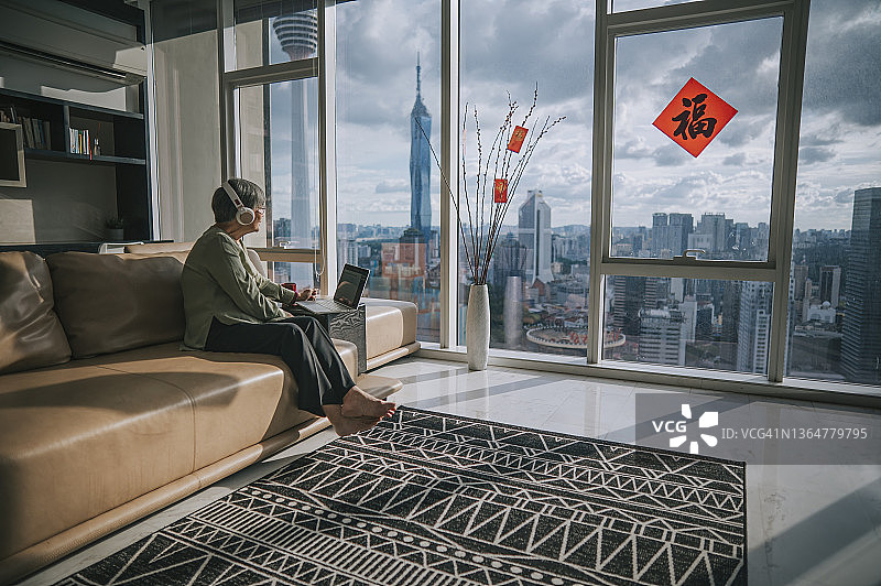 亚洲华人年长妇女使用笔记本电脑视频会议与她的家人在中国新年期间在她的公寓在城市的客厅图片素材