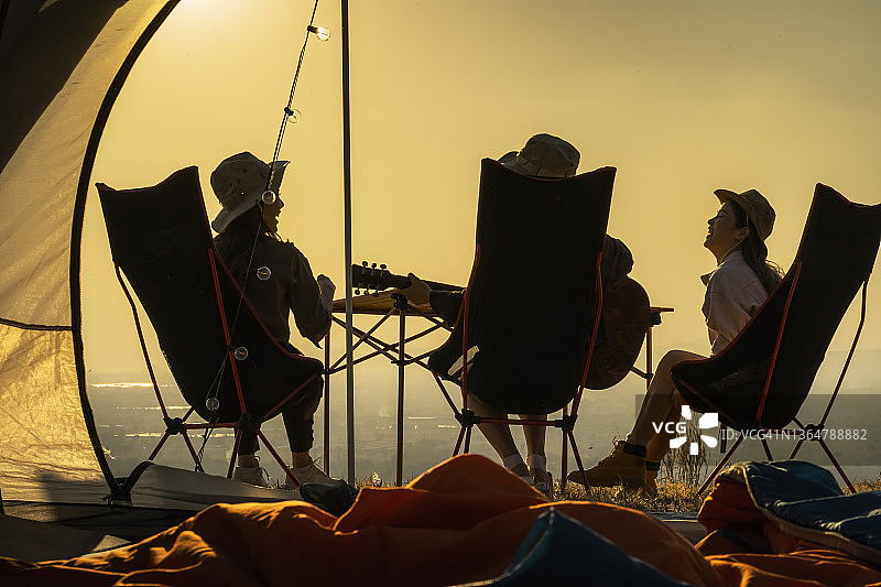一群年轻的亚洲朋友在帐篷里弹吉他唱歌，夏季露营度假，自由、休闲、旅行、冒险的概念图片素材