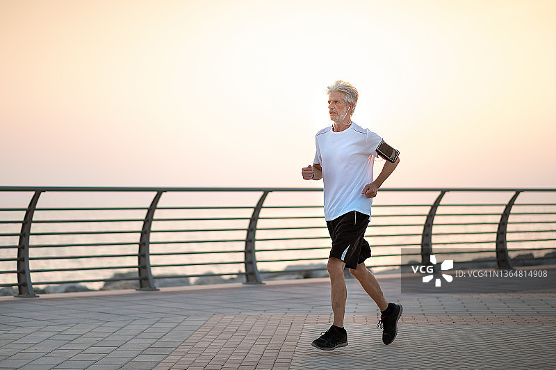 年长的男人在日落时分在海边跑步图片素材