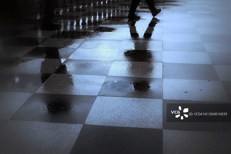人们倒影在湿漉漉的方格人行道上图片素材