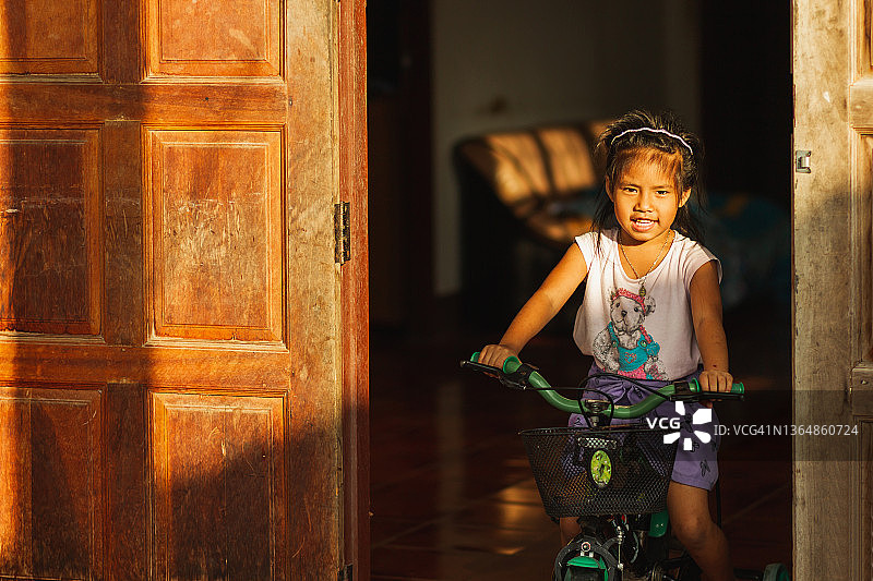 阳光下在家骑自行车的亚洲女孩的微笑肖像，童年图片素材