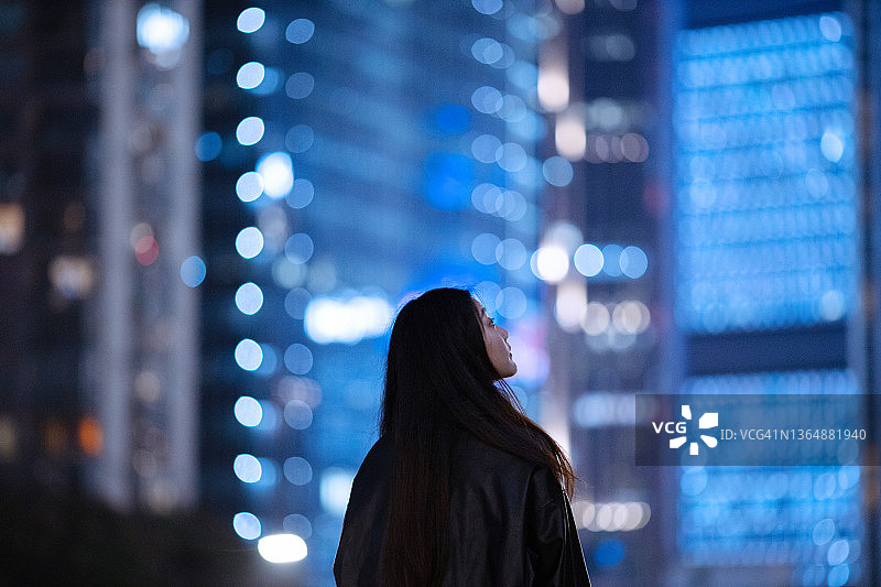 年轻的亚洲女性在城市摩天大楼下使用智能手机图片素材