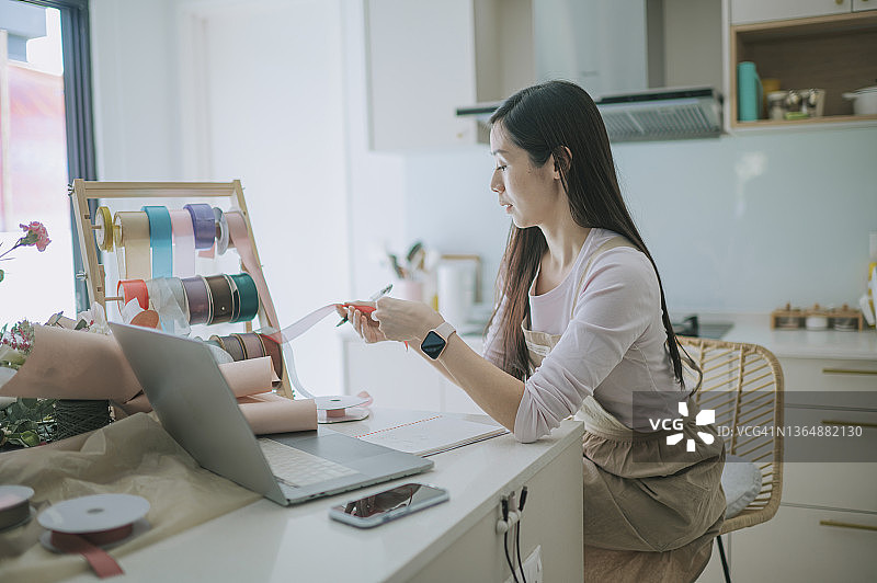 亚洲女花店主在笔记本电脑上工作，检查库存图片素材