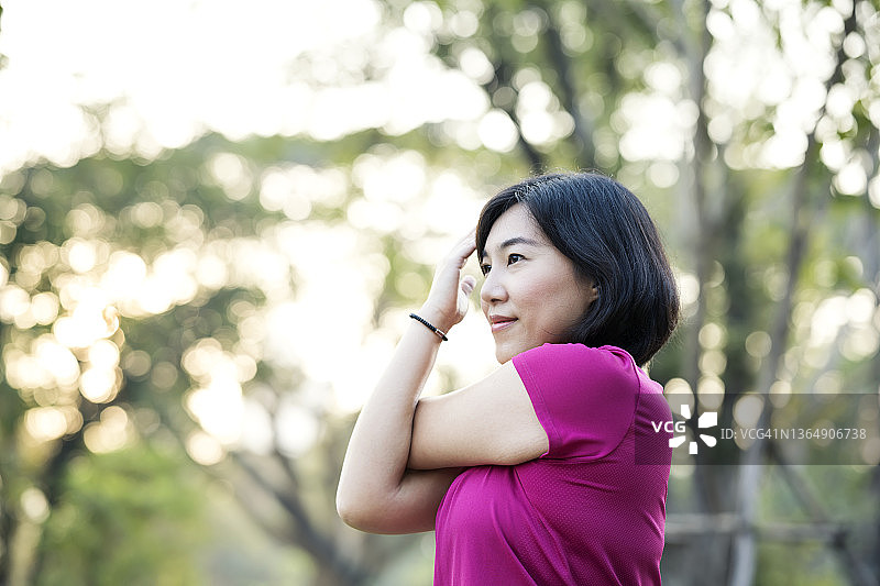 热身和放松伸展运动。快乐的亚洲女性跑步者在公园的跑道上晨跑前做肩部伸展运动图片素材