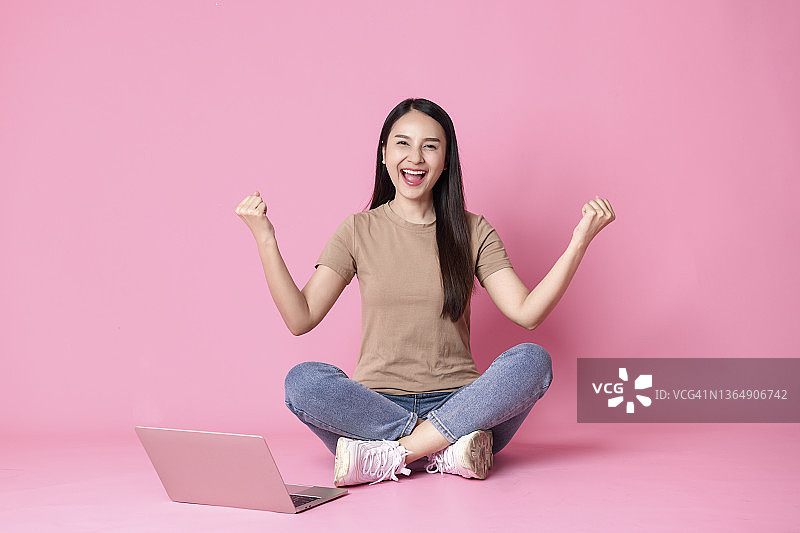 年轻亚洲女性坐在地板上使用笔记本电脑，庆祝成功图片素材