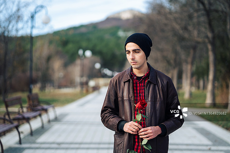 情人节，悲伤的年轻男子手持红玫瑰在公园等待女友图片素材