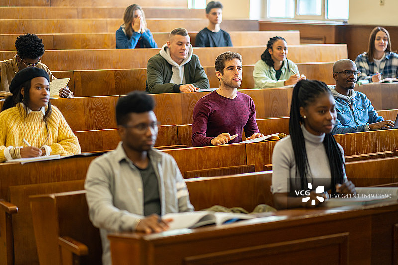 一群多民族大学生坐在阶梯教室里听教授讲课图片素材