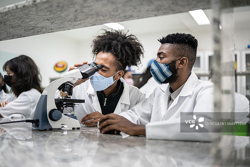 学生在实验室里戴着口罩看显微镜图片素材