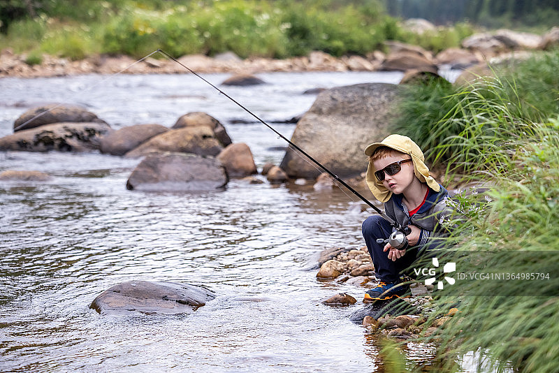 在魁北克河里钓鱼的可爱红发男孩图片素材