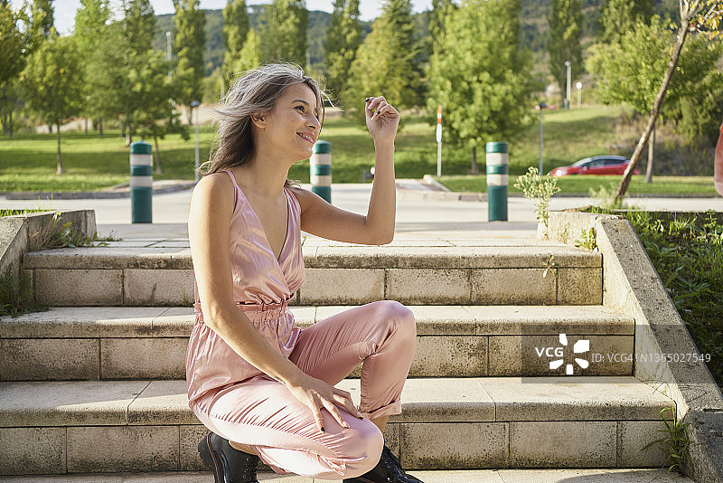 阳光明媚的日子里，蹲在楼梯上摆姿势拍照的年轻女子图片素材