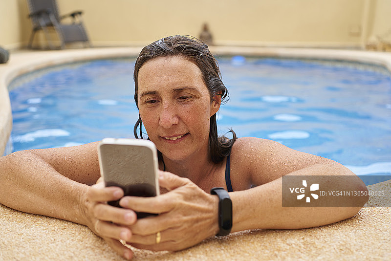 中年妇女在泳池边使用手机微笑，夏季假期视频通话图片素材