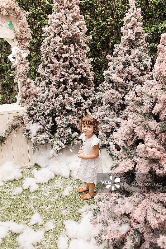 佛罗里达州棕榈滩，梦幻般的粉色圣诞树冬季仙境中，一个穿着白色连衣裙的两岁女童在玩耍图片素材