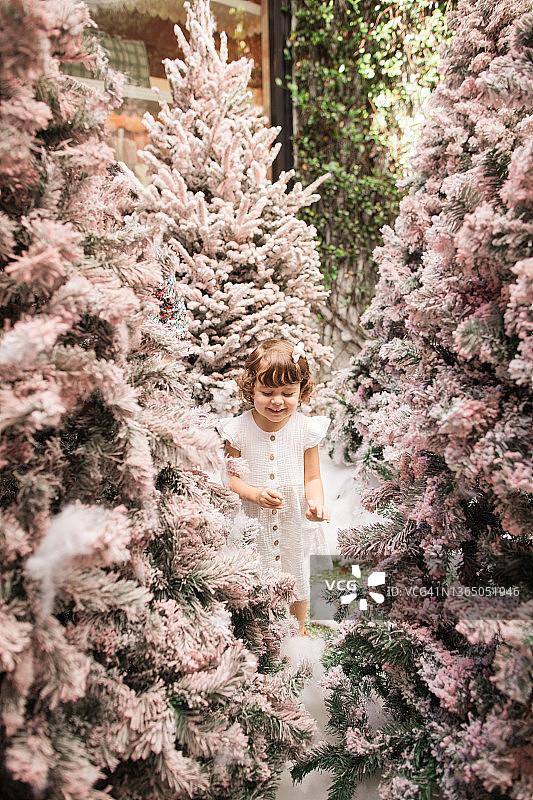 佛罗里达州棕榈滩，梦幻般的粉色圣诞树冬季仙境中，一个穿着白色连衣裙的两岁女童在玩耍图片素材