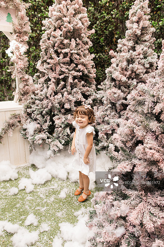 佛罗里达州棕榈滩，梦幻般的粉色圣诞树冬季仙境中，一个穿着白色连衣裙的两岁女童在玩耍图片素材
