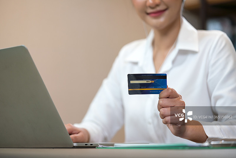 年轻女子拿着信用卡，用笔记本电脑在网上购物图片素材