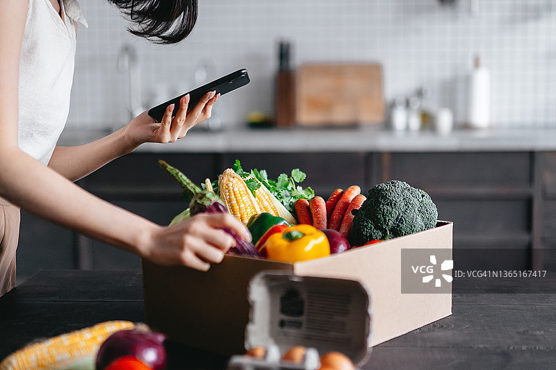 亚洲女人使用手机App在线购买杂货送货上门图片素材