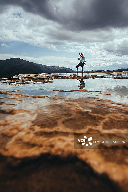 一位年轻摄影师站在水沸石边缘，欣赏壮丽的山景图片素材