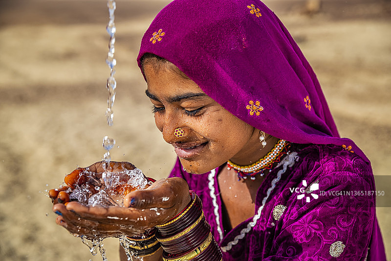 在印度拉贾斯坦邦沙漠村庄喝水的年轻印度女孩图片素材
