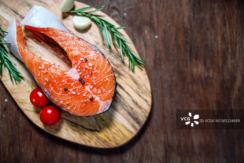 三文鱼：配有番茄、迷迭香和大蒜的生鳟鱼排，置于木桌上图片素材