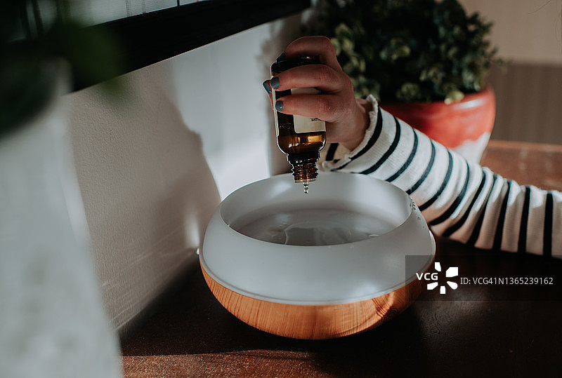 一个孩子将精油混合物添加到家用油扩散器中图片素材