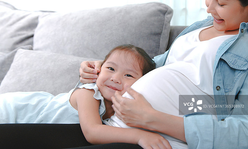 快乐的小女童拥抱她怀孕的母亲图片素材