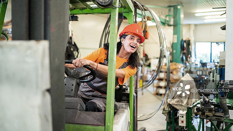 工厂里戴着防护头盔的中年女工，在仓库里驾驶叉车图片素材