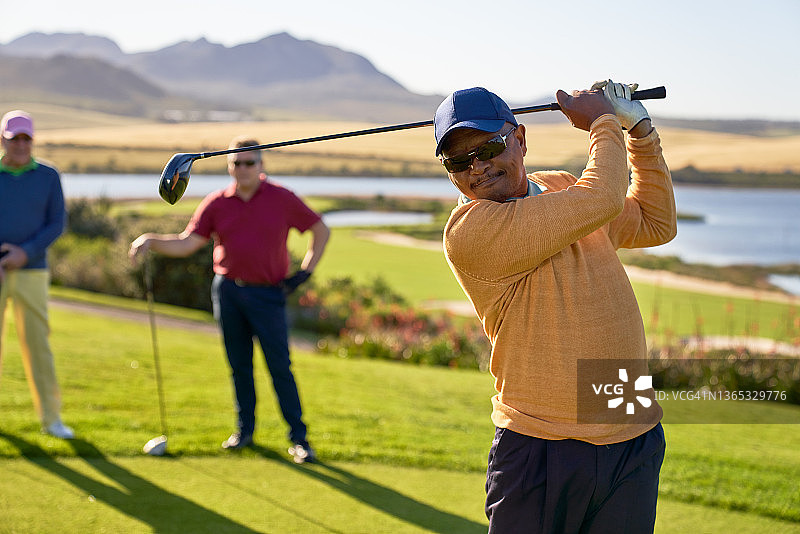 在阳光明媚的发球区开球的中年男高尔夫球手图片素材