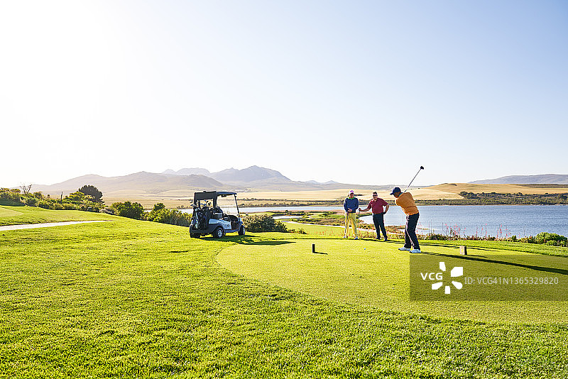 阳光明媚的湖边，高尔夫球手开球图片素材