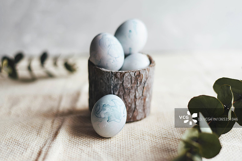 浅色背景小篮子里的蓝色复活节彩蛋。复活节彩蛋设计。浅色天然织物。木制篮子。绿色树枝。复活节。浅色背景。图片素材
