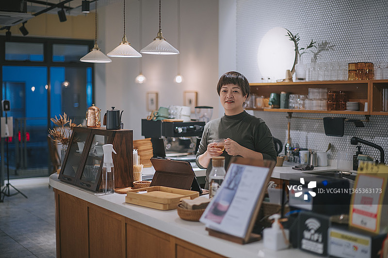 小商店主在厨房柜台拿着茶杯微笑看着镜头图片素材
