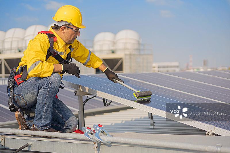男工程师在高楼顶上清洁光伏板系统。图片素材