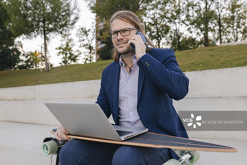 在台阶上用手机交谈的滑板电脑商人图片素材