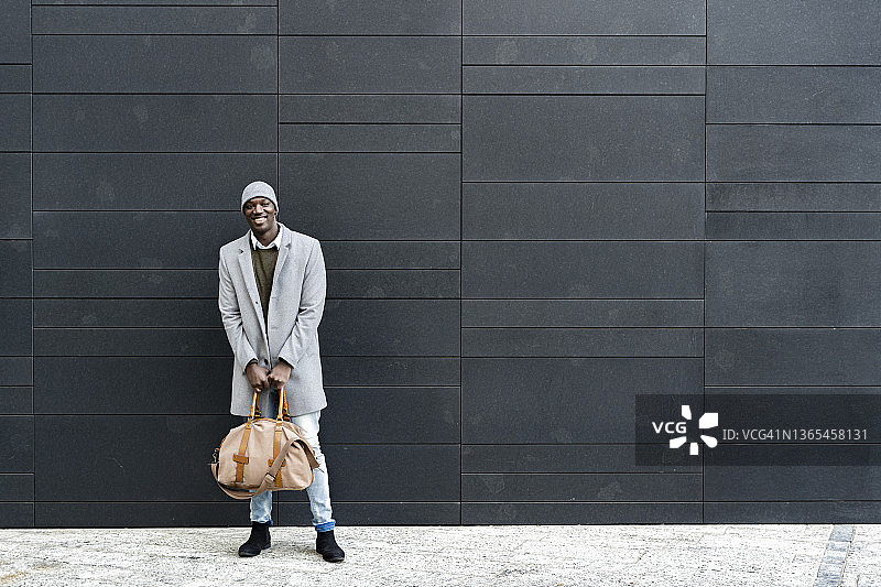 带着旅行包站在黑色墙前的微笑男士图片素材