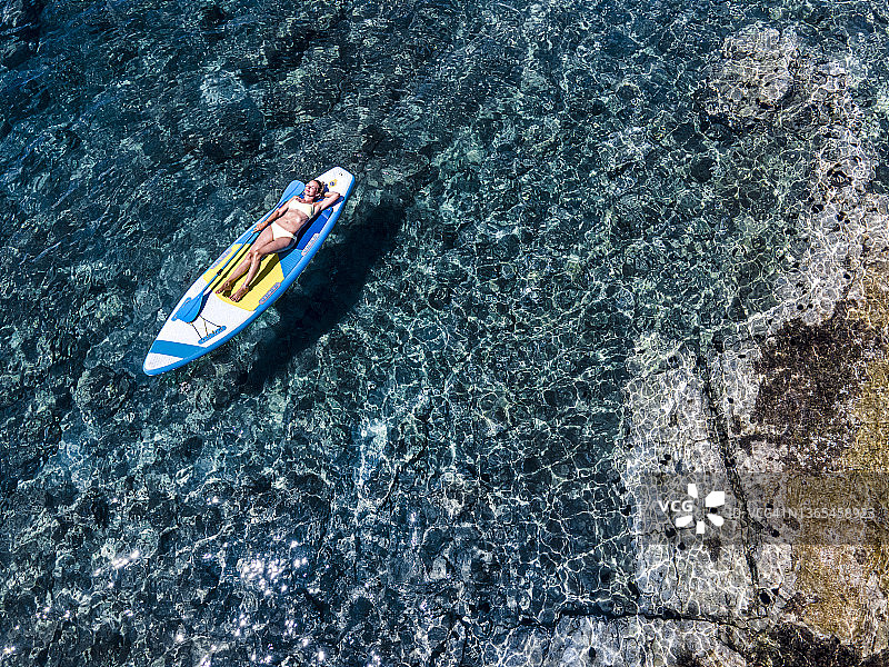中年妇女在度假时穿着比基尼躺在海上桨板上图片素材