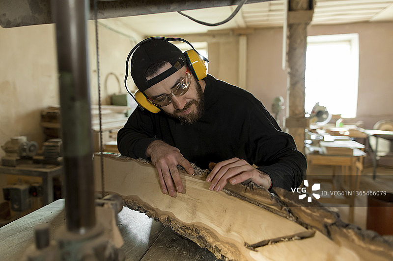 戴着耳罩的工匠在车间通过带锯雕刻木头图片素材