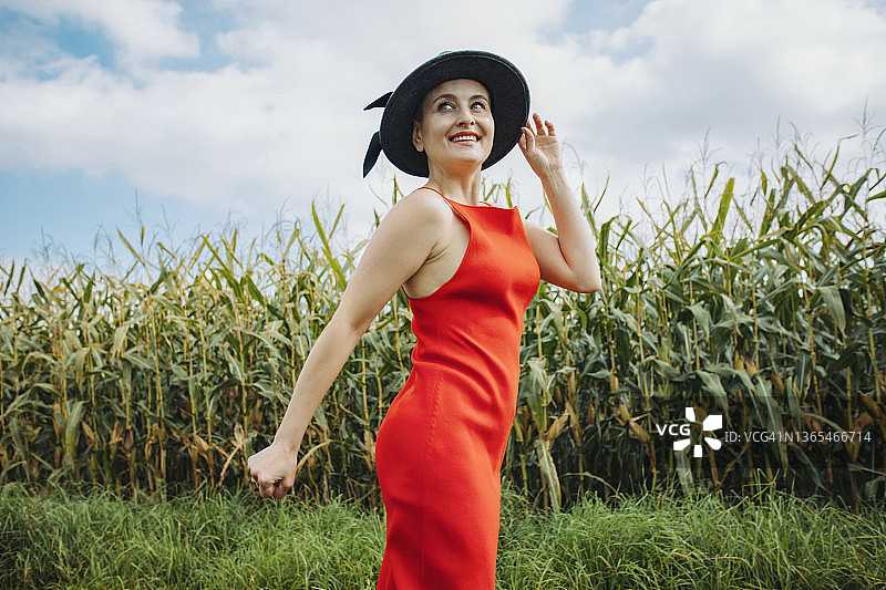 戴着帽子站在玉米地前的微笑美丽女人图片素材