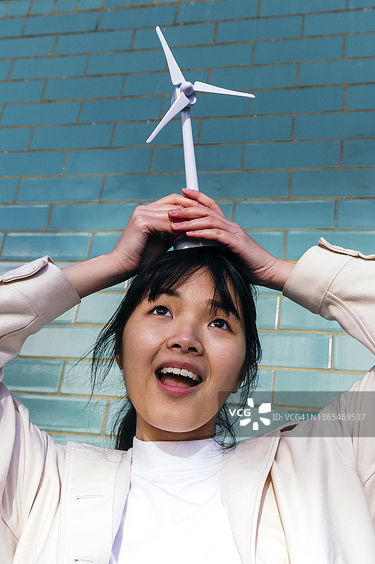 在砖墙前头顶风力涡轮玩具的年轻女性图片素材