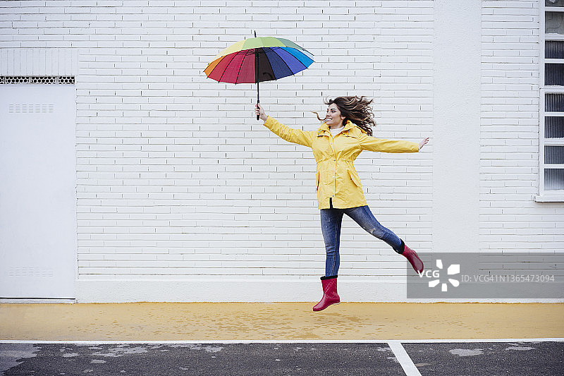 快乐的女人在路上跳跃，手持雨伞图片素材
