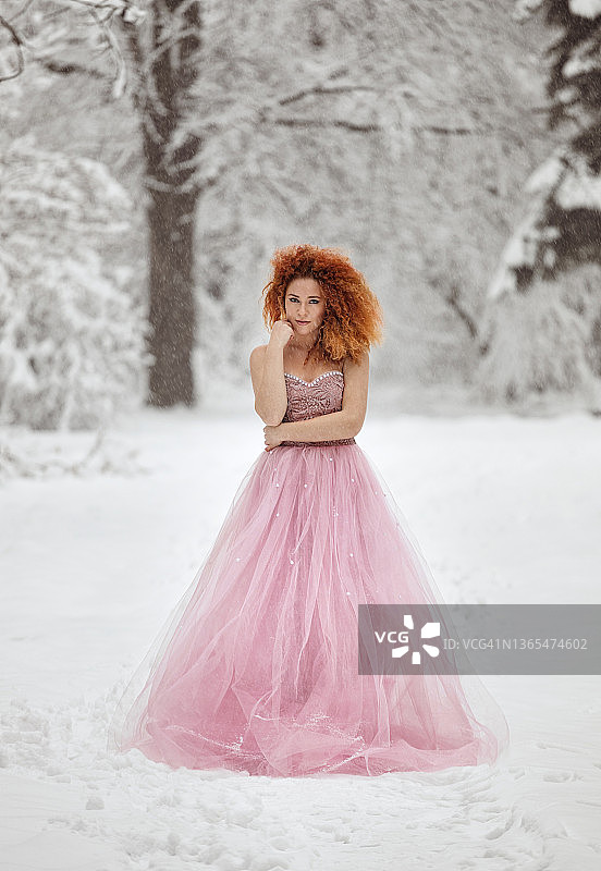 冬季童话：一位身穿粉色连衣裙的年轻女子在白雪皑皑的森林里享受美景图片素材