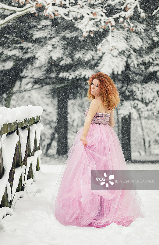 冬季童话：一位身穿粉色连衣裙的年轻女子在白雪皑皑的森林里享受美景图片素材
