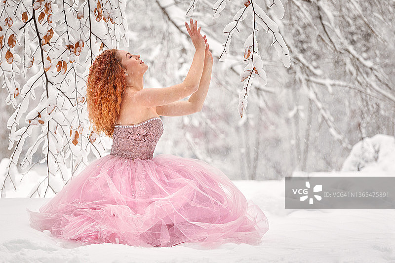 冬季童话：一位身穿粉色连衣裙的年轻女子在白雪皑皑的森林里享受美景图片素材