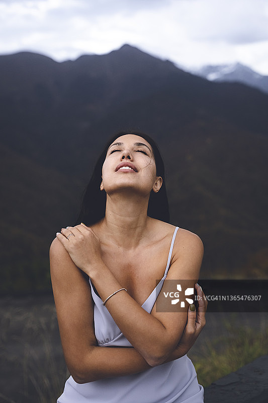 在山前闭着眼睛拥抱自己的性感年轻女子图片素材