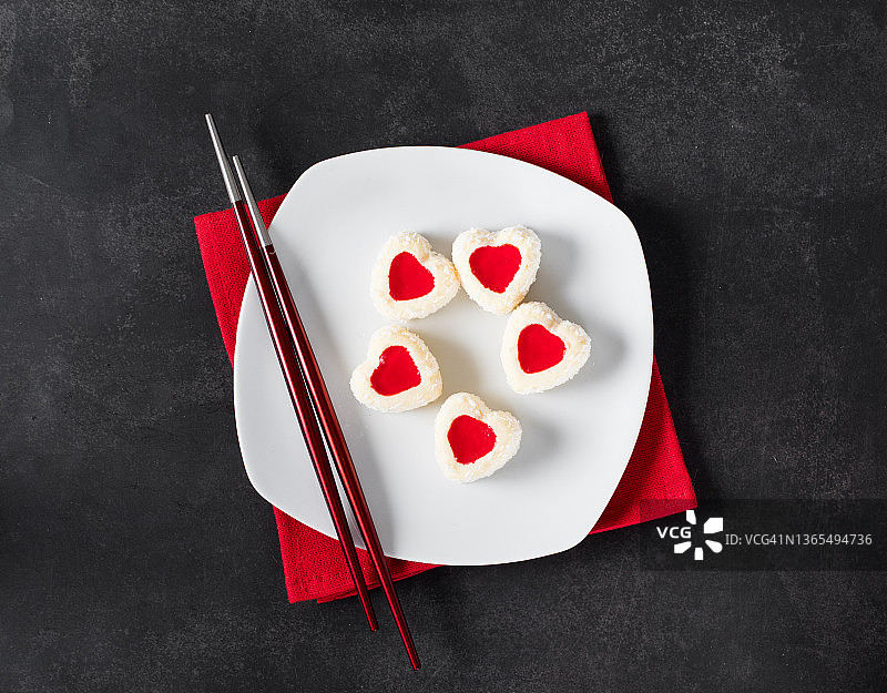 心形慕斯白巧克力奶油蛋糕，草莓果冻馅，撒上椰子片，放在深灰色背景的餐盘上。顶视图。情人节图片素材