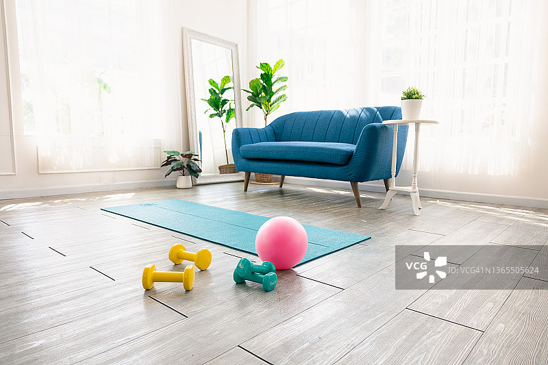 家用健身房地板上的瑜伽垫、健身球和哑铃图片素材