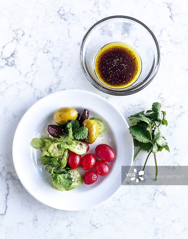 白色大理石背景上的番茄黄瓜橄榄沙拉和油醋汁图片素材