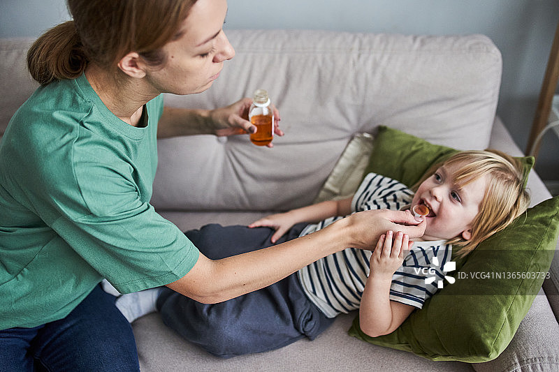 年轻的母亲在家为孩子治疗咳嗽，喂一勺止咳药图片素材