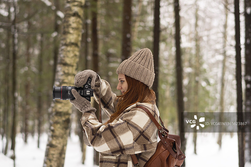 女子在冬季度假时于森林中用相机拍照图片素材