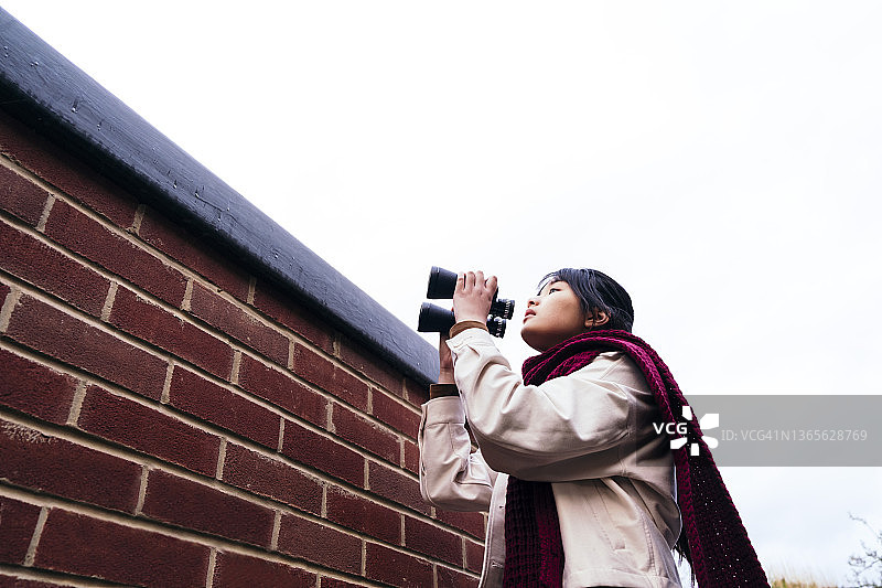 站在砖墙附近手持双筒望远镜的女人图片素材
