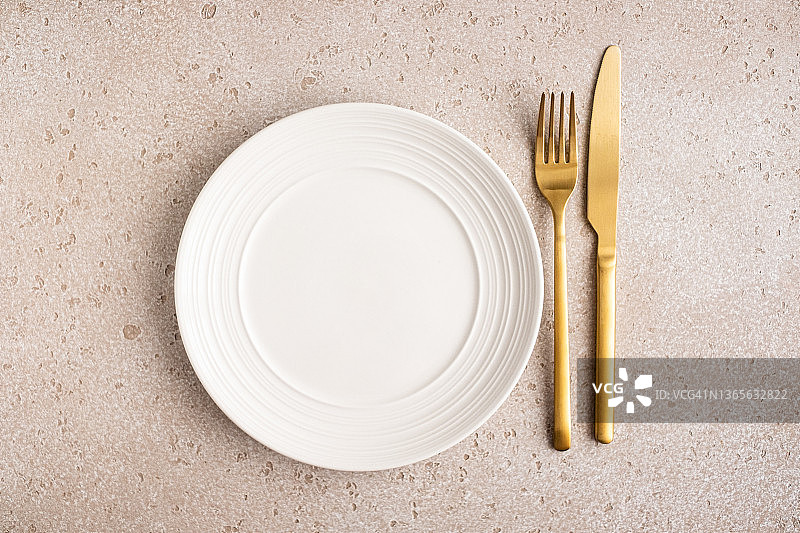 粉色水泥背景上的空白白色陶瓷盘与金色刀叉俯视图图片素材